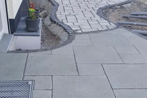 Ein sauber verlegter Pflasterweg aus hellgrauen Steinplatten mit geschwungenem Rand.