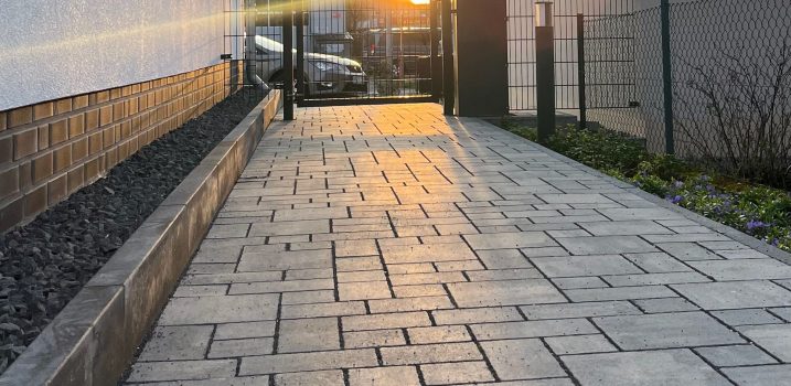Geradliniger Pflasterweg mit dezenter Beleuchtung.